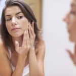 young woman with acne problem looking in mirror