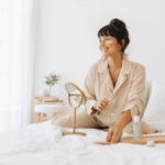 Woman doing skin care massage sitting on bed, Smiling woman using a roller to massage face.