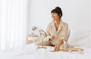 Woman doing skin care massage sitting on bed, Smiling woman using a roller to massage face.