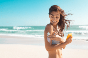 Beautiful young latin woman applying suntan lotion at sea with copy space.