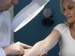 Dermatologist examining the arms of female patient in clinic