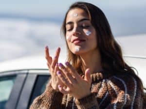 woman applying a sunscreen on her face in snowy mountains in winter